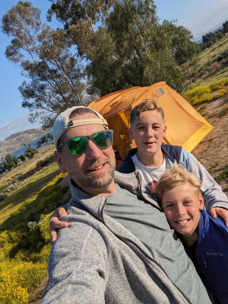 A man and his children enjoying a camping trip in front of a tent.
